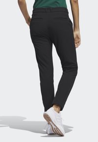 Svarta slim-fit byxor med en slät yta, utrustade med två bakfickor. Bärs med vita sneakers, vilket betonar en ren och modern stil.