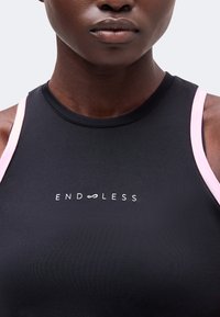 Gros plan d'une personne portant un haut noir sans manches avec des bretelles roses et le mot "ENDLESS" en lettres blanches sur la poitrine.