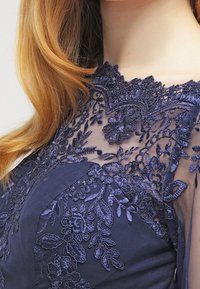 Granatowa sukienka z misternym haftem kwiatowym na przezroczystych rękawach, z teksturowanym korpusem i wysokim dekoltem.