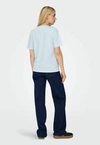 Lys blå bomulds t-shirt med korte ærmer, parret med mørk blå løsthængende jeans. Synlig syning og brune sneakers.