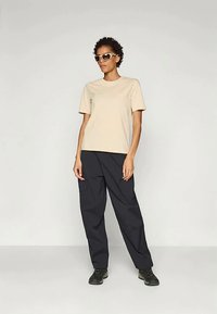 Šviesiai rudos spalvos medvilninė marškinėlių, derinami su plačiais juodais kelnais, dėvima su dideliais šviesiais saulės akiniais ir juodais sportbačiais.