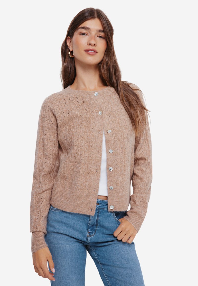 Beige gebreide cardigan met een ronde halslijn en knoopsluiting, voorzien van een gemêleerd patroon en geribde manchetten. Gekocht over een witte top.