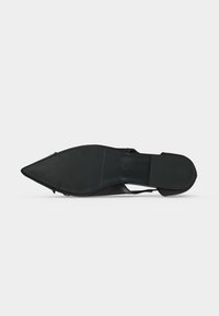 Semelle de chaussure noire à bout pointu, avec un avant lisse et un talon texturé, vue de dessous sur un fond clair uni.