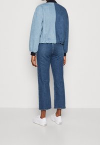 Kurtka dżinsowa ma wzór w blokach kolorystycznych z jasnoniebieskimi i ciemnoniebieskimi sekcjami, łączona z pasującymi spodniami dżinsowymi o wysokim stanie oraz białymi trampkami.