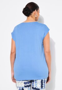 Blå kortärmad topp med avslappnad passform, med en mjuk textur. Bärs med mönstrade byxor som visar en geometrisk design i blått och krämfärgat.