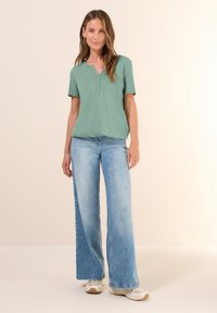 Haut vert menthe à manches courtes avec un décolleté en V et une coupe décontractée, associé à un jean en denim à jambes larges bleu clair. Des chaussures décontractées complètent le look.