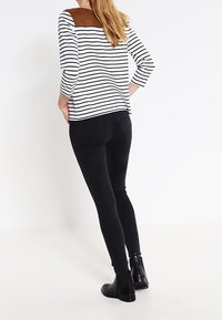 Randig svart och vit topp med trekvartslånga ärmar, brun mockaaccent på axeln, kombinerad med svarta smala jeans och ankelboots.