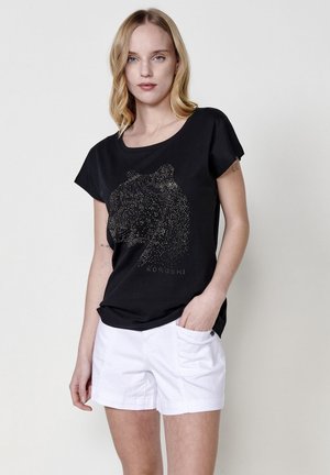 Camiseta de algodón negra con un diseño de león brillante. Manga corta, cuello redondo, combinada con pantalones cortos blancos, mostrando un estilo casual.