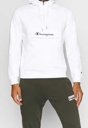 Sudadera con capucha blanca de tela suave, con cremallera en el cuello, parche central con logo y puños acanalados. Combinada con pantalones jogger de color verde oliva.