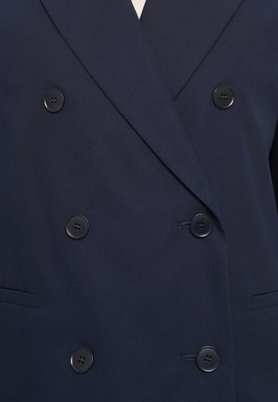 Blazer doppiopetto navy con grandi bottoni neri, sagomato, con rever a puntino e tasche laterali. Tessuto liscio e texture.