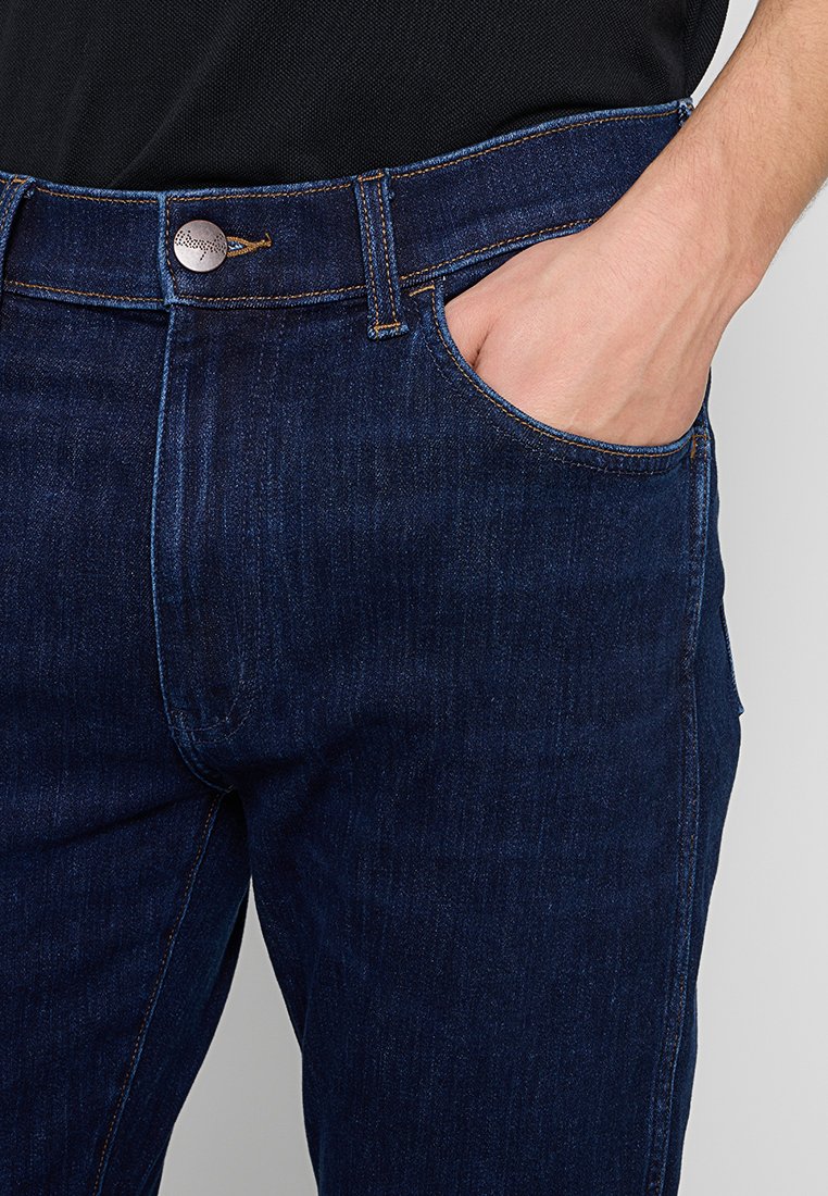 Dunkelblaue Jeans aus Denim mit einem klassischen geraden Schnitt, ausgestattet mit einem Metallknopfverschluss, sichtbaren Nähten und einer Fronttasche.