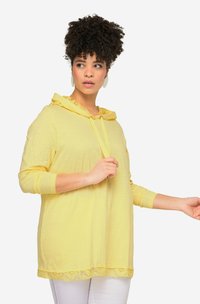 Žlutá mikina s krajkovým lemem, dlouhými rukávy a předním stahováním. Vyrobena z lehkého materiálu, s uvolněným střihem.