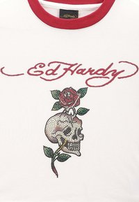 Hvid t-shirt med en rød rund halsudskæring, der prydes af et design med et skelet og en rose lavet af farvede krystaller. "Ed Hardy" logo i rødt over grafikken.