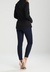 Chemise noire à boutons, pantalon ajusté bleu marine et chaussures à talons hauts couleur nude. Tissu lisse et coupe ajustée, avec un ourlet arrondi à l'arrière.