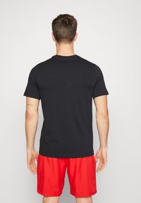 Camiseta de algodón negra con mangas cortas, escote redondo y corte recto, combinada con shorts deportivos rojos. Textura suave, sin patrones.