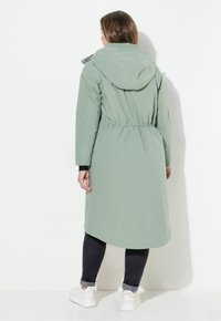 Cappotto impermeabile lungo, di colore verde chiaro, con cappuccio, vita elastica e due tasche laterali, caratterizzato da una texture liscia e design a lunghezza intera.