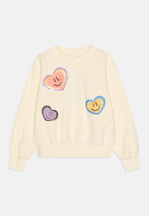 Sweatshirt de couleur crème avec des poignets et un ourlet côtelés. Présente quatre motifs de cœurs en sequins colorés en rose, violet et bleu.