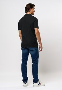 Zwarte polo met korte mouwen en ribgebreide kraag. Gecombineerd met blauwe spijkerbroeken en witte sneakers met rode en marineblauwe accenten.