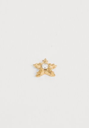 Petit ornement doré en forme d’étoile avec une surface texturée et une pierre précieuse ronde claire sertie au centre sur fond blanc.