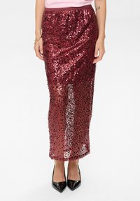 Gonna maxi in paillettes bordeaux con una cintura elasticizzata, caratterizzata da una vestibilità slim e sezioni trasparenti. Abbinata a tacchi a punta neri.