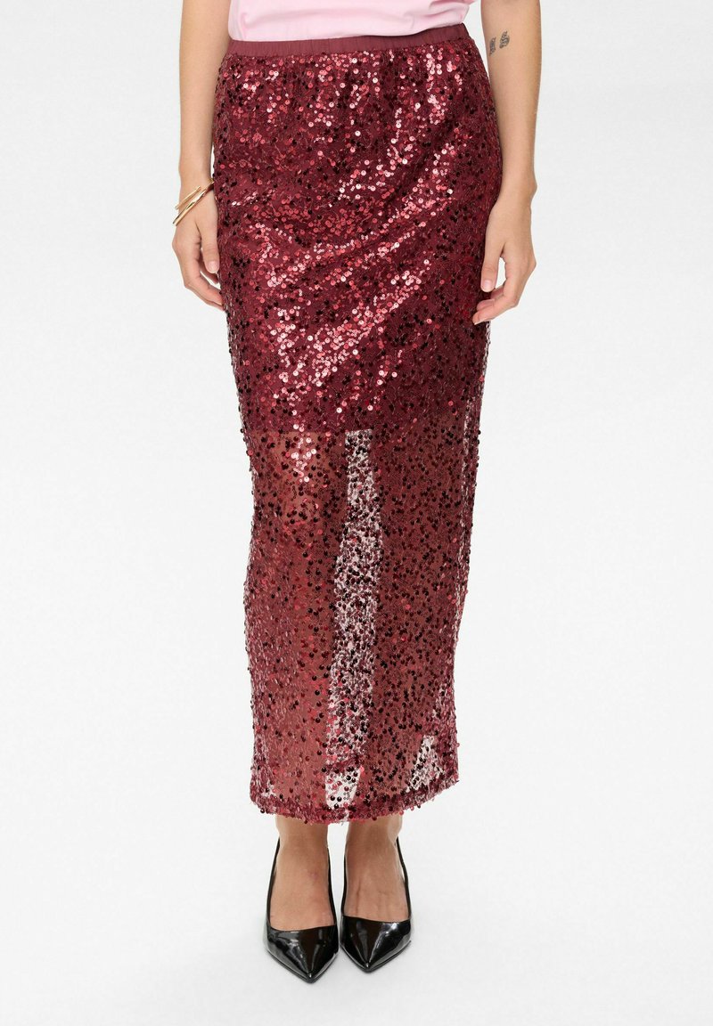Gonna maxi in paillettes bordeaux con una cintura elasticizzata, caratterizzata da una vestibilità slim e sezioni trasparenti. Abbinata a tacchi a punta neri.