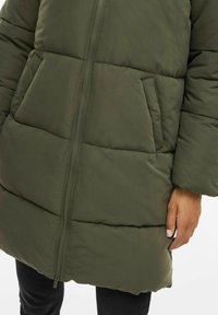 Giacca a vento color verde oliva con zip frontale, design trapuntato orizzontale, tasche laterali e vestibilità morbida. Tessuto testurizzato e finitura morbida.