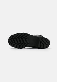 Suola di stivale in gomma nera con profondi battistrada, caratterizzata da un tacco piatto e motivi testurizzati per una migliore aderenza. Logo del marchio impresso sul lato.