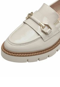 Mocassin en cuir beige clair avec une finition brillante, comportant une boucle décorative en or et une semelle en liège texturée avec une épaisse plateforme.