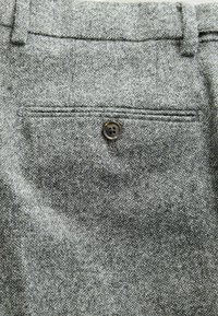 Gray wool trousers feature a textured fabric with a back pocket adorned with a dark brown button. Tailored design with belt loops.