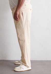 Lichtbeige broek van katoen, met een iets relaxte pasvorm, zijzakken en een gladde textuur. Gecombineerd met witte sneakers.