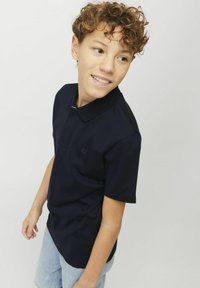 Marinblå polo-shirt med texturerad krage och korta ärmar, med en liten logotyp på bröstet. I kombination med ljusa denimshorts.