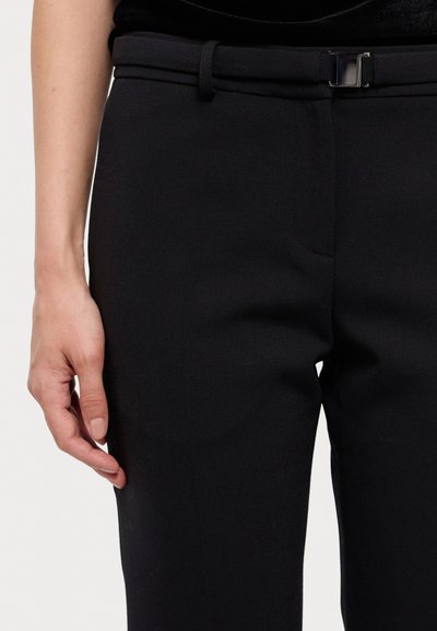 calças pretas sob medida feitas de tecido texturizado, apresentando um corte slim, bolsos laterais e um cinto simples com uma fivela metálica retangular.