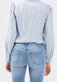 Chemise bleu clair à boutons avec manches bouffantes, associée à un jean en denim bleu clair avec deux poches arrière et une coupe ajustée.