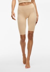 Leggings beige hasta la rodilla con una cintura alta, hechos de un material suave y elástico, con un diseño simple y sin patrones visibles.