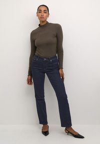 Un jean bleu foncé avec une coupe droite, associé à un haut à manches longues en olive côtelé. Des chaussures noires à bout pointu complètent la tenue.
