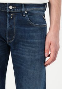 Dark blue denim jeans with a straight cut, featuring a button closure, belt loops, and subtle fading. Includes five pockets with stitching details.