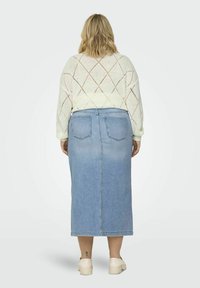 Falda midi de denim azul claro con corte recto y dos bolsillos traseros, combinada con un suéter crema de punto trenzado que presenta patrones en forma de diamante.