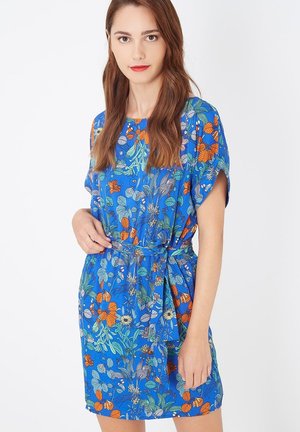 Vestido corto floral en azul con patrones en naranja, verde y amarillo. Corte holgado, mangas cortas y un cinturón de lazo en la cintura.