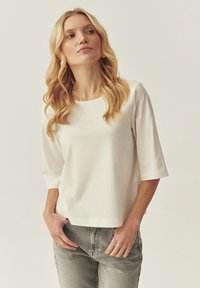 Haut blanc à manches courtes avec un col rond et une coupe décontractée, fabriqué en tissu lisse. Associé à un jean gris taille haute.