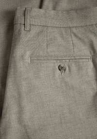 Lichtgrijze broek met een gemêleerde stof, voorzien van een achterzak die met een knoop is vastgezet en ceintuurlussen bij de taille.