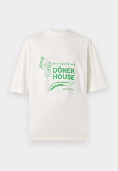 Λευκό μπλουζάκι με πράσινο γραφικό ενός ντονέρ κεμπάμπ, το κείμενο "Han Kjøbenhavn Döner House" και έναν αριθμό τηλεφώνου στο κέντρο μπροστά.