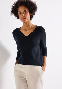Navy geribbelde trui met een V-hals, lange mouwen en een relaxte pasvorm, gecombineerd met lichtgekleurde, gestructureerde broek.