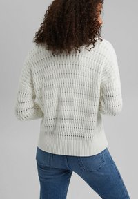 Vit stickad tröja med ett texturerat mönster och öppna vävdetaljer, ribbat fåll och långa ärmar. Matchad med blå jeans.