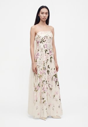 Femme portant une robe bustier longue jusqu'au sol avec une broderie florale en sequins roses, verts et blancs sur tissu transparent.