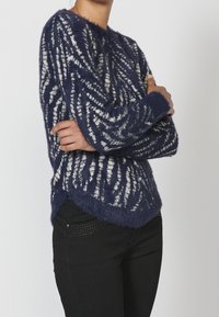 Jersey azul marino de gran tamaño con patrón de zigzag blanco, hecho de material suave, con cuello redondo y diseño de dobladillo asimétrico.
