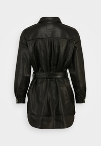 Musta nahkapaita, jossa on kauluksellinen kaula, pitkät hihat, vyötärölle sidottu vyö ja kerätty yksityiskohta selässä. Sileä pinta ja hyvin istuva leikkaus.