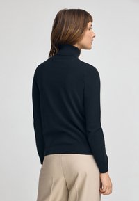 Svart polotröja i mjukt stickad tyg, figursydd design med långa ärmar, ribbat krage och avslut.