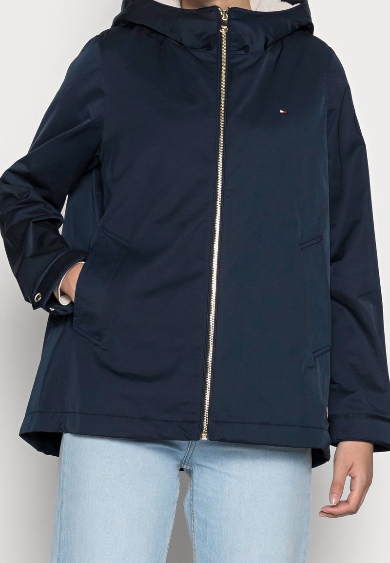 Mörkblå huvad jacka med dragkedja, utrustad med två framfickor och en mjuk foder. Dekorerad med en liten logotyp på bröstet.