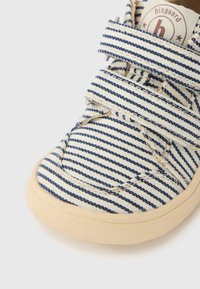 Ριγέ καμβάς παπούτσι σε μπλε και λευκό, με λουράκια βέλκρο, στρογγυλεμένη μύτη και υφασμένο καουτσούκ σόλα σε ανοιχτό καφέ χρώμα.