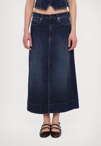 Mörkblå denimmaxikjol med rak skärning, fem fickor och sömnadsdetaljer. Matchad med mörka skor med remmar.